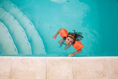 Ein Mädchen schwimmt sicher mit Schwimmflügeln im Pool.