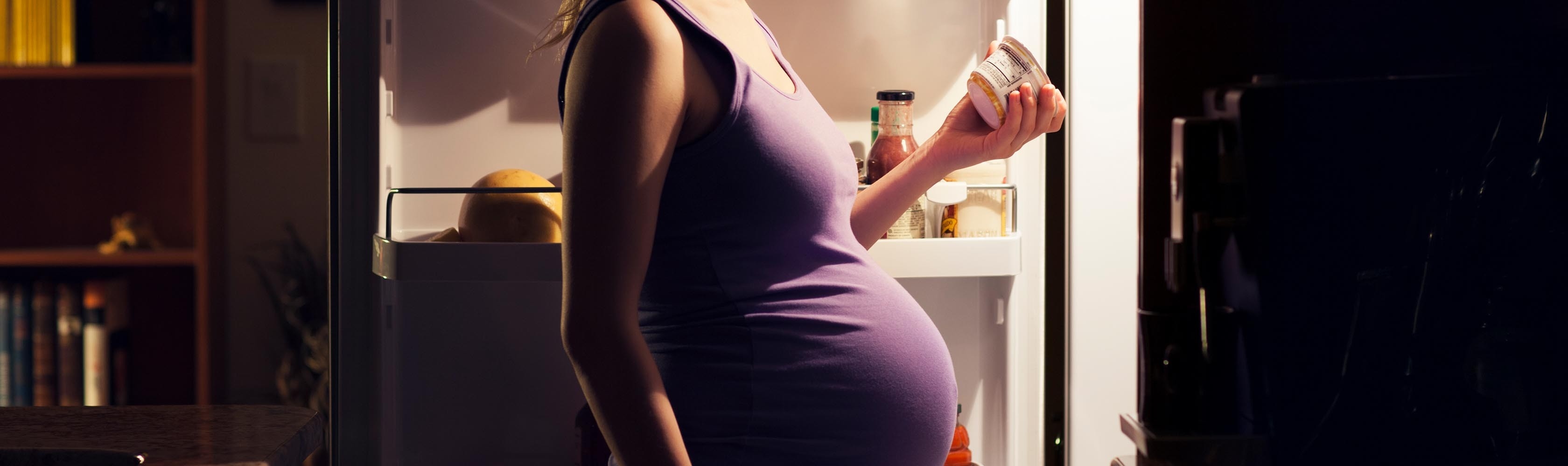 Ernährung während der Schwangerschaft – Schwangere Frau steht nachts vor dem Kühlschrank.