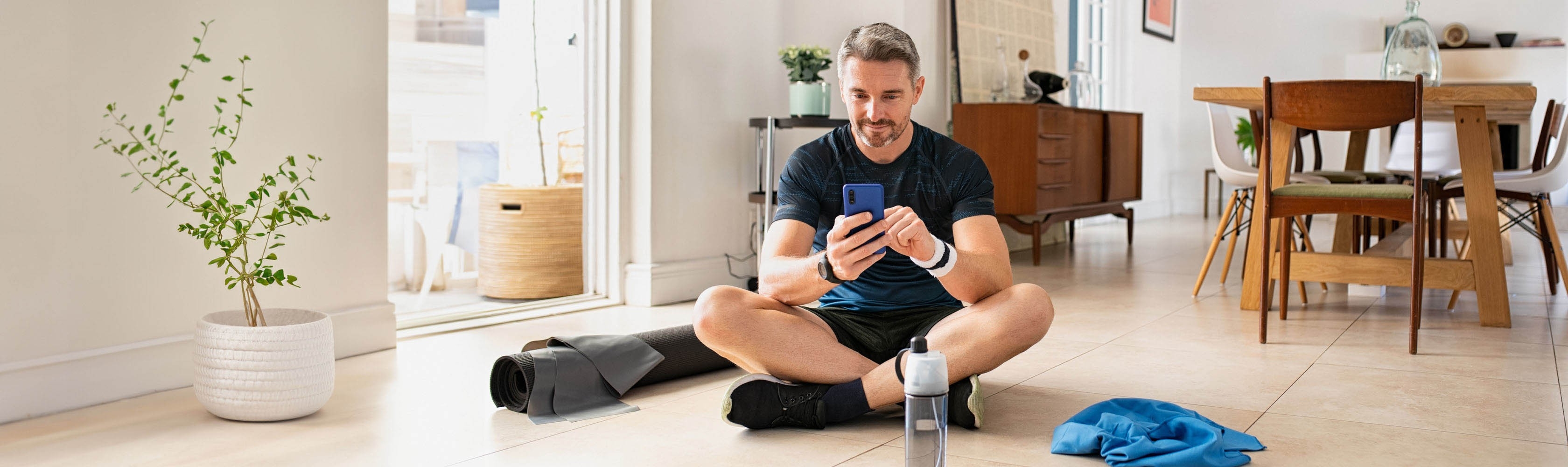 A sporty man is sitting on the ground with his smartphone and using an app.
