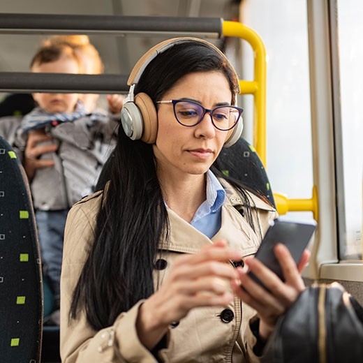 A young woman with glasses and headphones listens to a health podcast on the bus