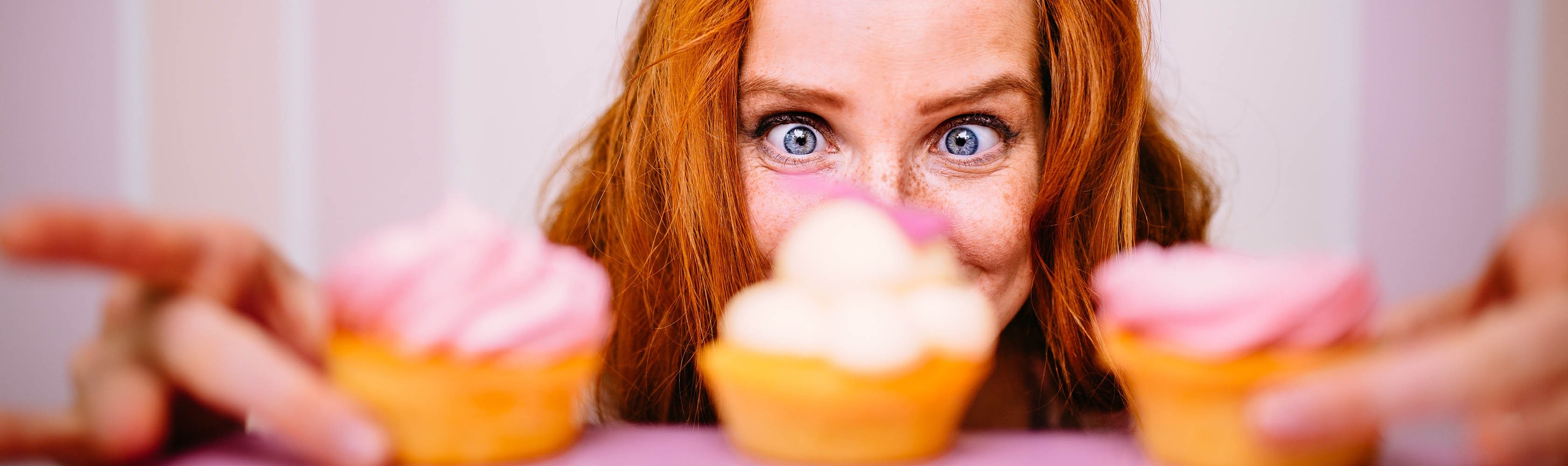 Une femme a trois cupcakes devant elle et tente de résister au désir.