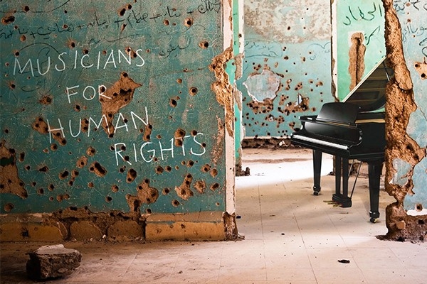 Sur un mur vert d’une vieille maison criblée d’impacts de balles, on peut lire l’inscription «Musicians for Human Rights». En arrière-plan, un piano attend les musicien·nes.