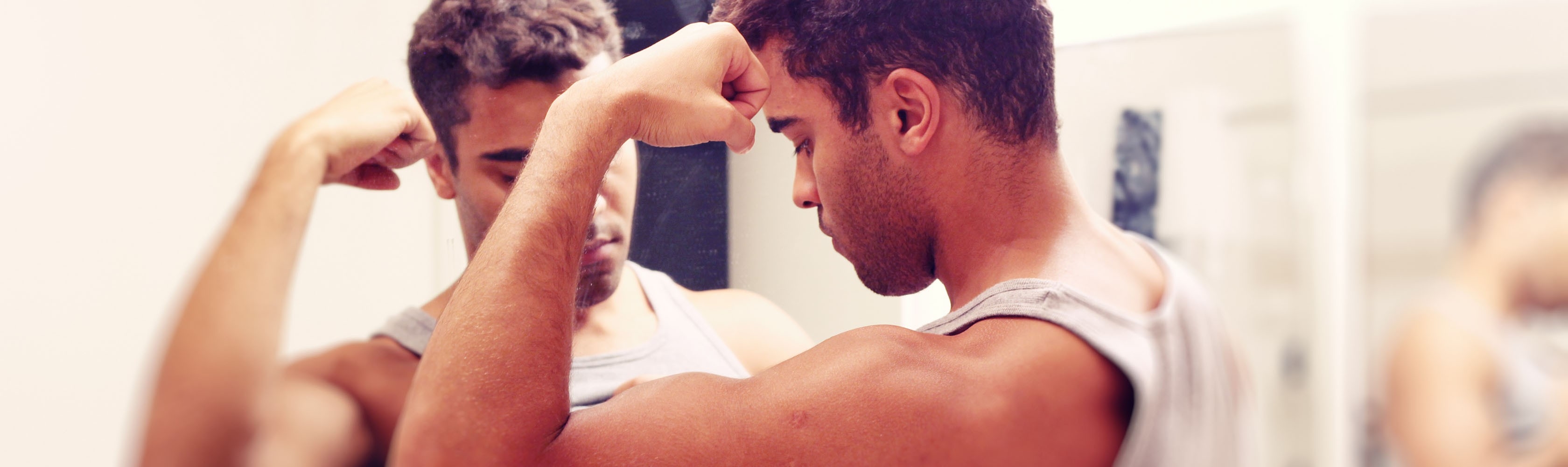 Un jeune homme regarde les muscles de son bras dans un miroir.